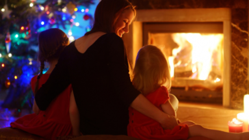 Mother sitting in front of fireplace and Christmas tree with children