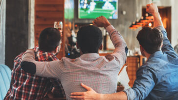 Three men watching football on TV in sport bar, back view