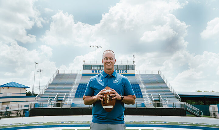 Coach Jeff Conaway holding a football, standing in the middle of the TFA football field.