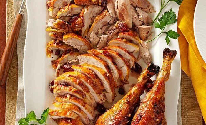 Sliced turkey on a white dish with two turkey legs and parsley garnish.