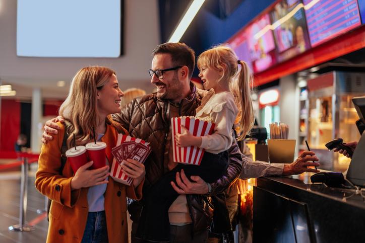 Two parents at the movie theater with their child, excited to see a movie on National Cinema Day.