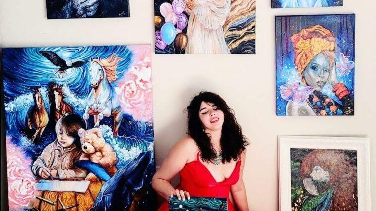female artist sitting on the floor, surrounded by her paintings