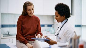 African American doctor and her female patient analyzing medical report after examination in the hospital. Focus is on female patient.