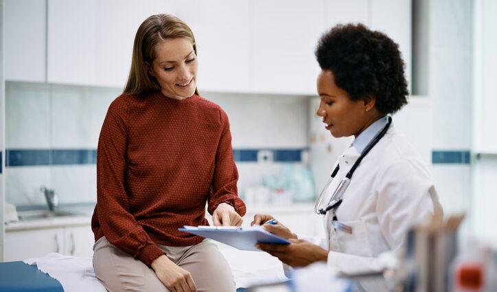African American doctor and her female patient analyzing medical report after examination in the hospital. Focus is on female patient.