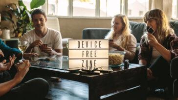 group of friends playing cards indoors at device free zone. Cell phones on table with young men and woman hanging out together. holiday detox