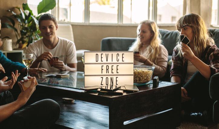 group of friends playing cards indoors at device free zone. Cell phones on table with young men and woman hanging out together. holiday detox