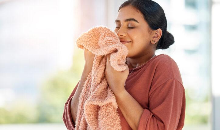 Woman smelling clean laundry, blanket or fabric for fresh and clean smell in house after doing washing, cleaning and housekeeping. Happy female cleaner with textile for aroma, fragrance and scent bath and body works
