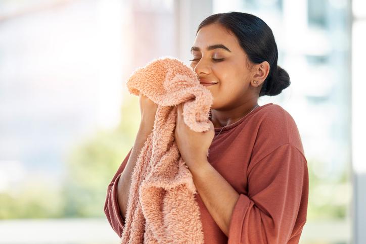 Woman smelling clean laundry, blanket or fabric for fresh and clean smell in house after doing washing, cleaning and housekeeping. Happy female cleaner with textile for aroma, fragrance and scent bath and body works