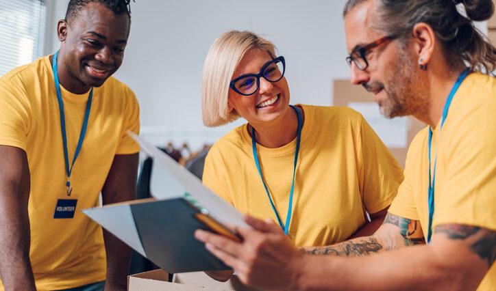 Group of diverse people working in charitable foundation. Happy volunteer separating donation stuff. Social workers making check list of the thins that are done. Copy space. Working as a team. giving guide.