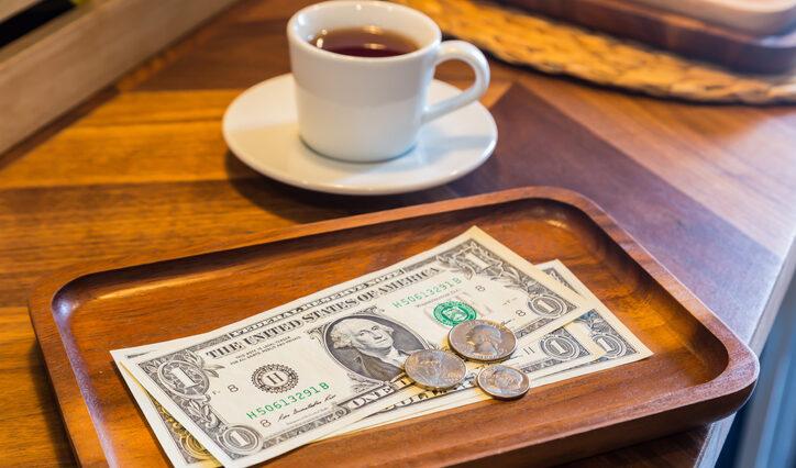 Dollar bills, coins and coffee on a table to represent the concept of tipping culture.