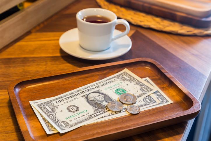 Dollar banknotes and coins money tips - Central Florida Lifestyle Dollar bills, coins and coffee on a table to represent the concept of tipping culture.