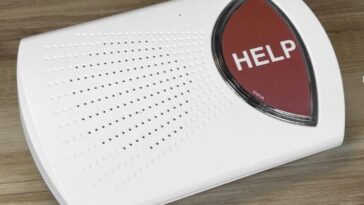 A white medical alert base unit with a prominent red help button on a clean surface