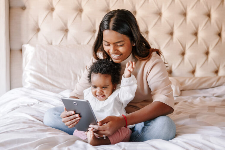 Mixed race Indian black mother with toddler baby girl watching cartoons on tablet Ethnic diversity Family mom with kid using technology Video chat video call Black people community Central Florida Lifestyle